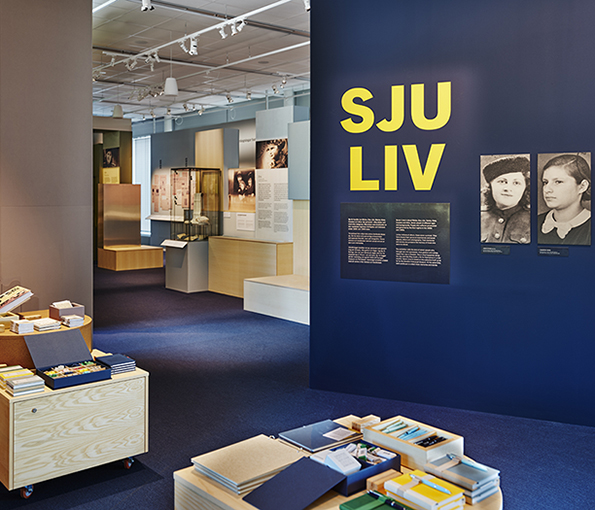 Museibutiken med vy in mot utställningen Sju liv, i förgrunden syns böcker på låga bord