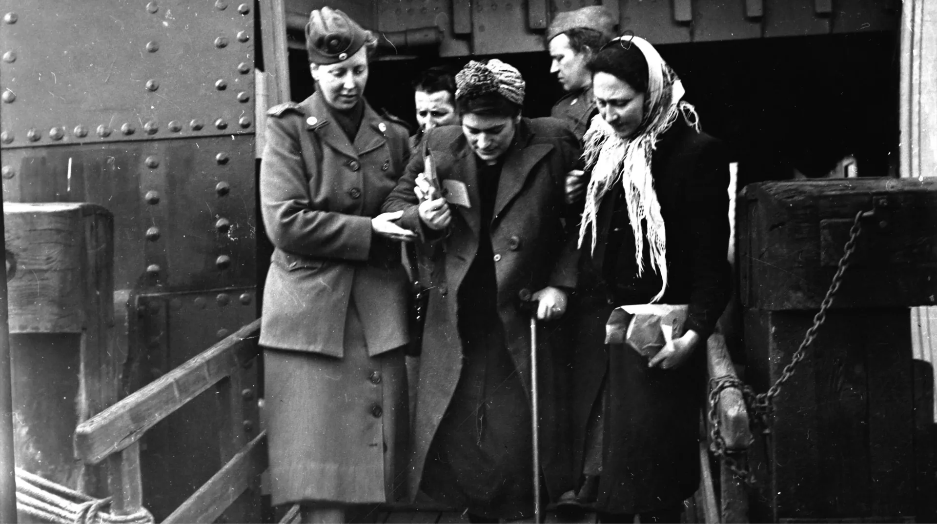 Judiska polska flyktingar från tyska koncentrationsläger kommer till Malmö 30 april 1945. En kvinna med käpp får hjälp av två personer för att ta sig fram.