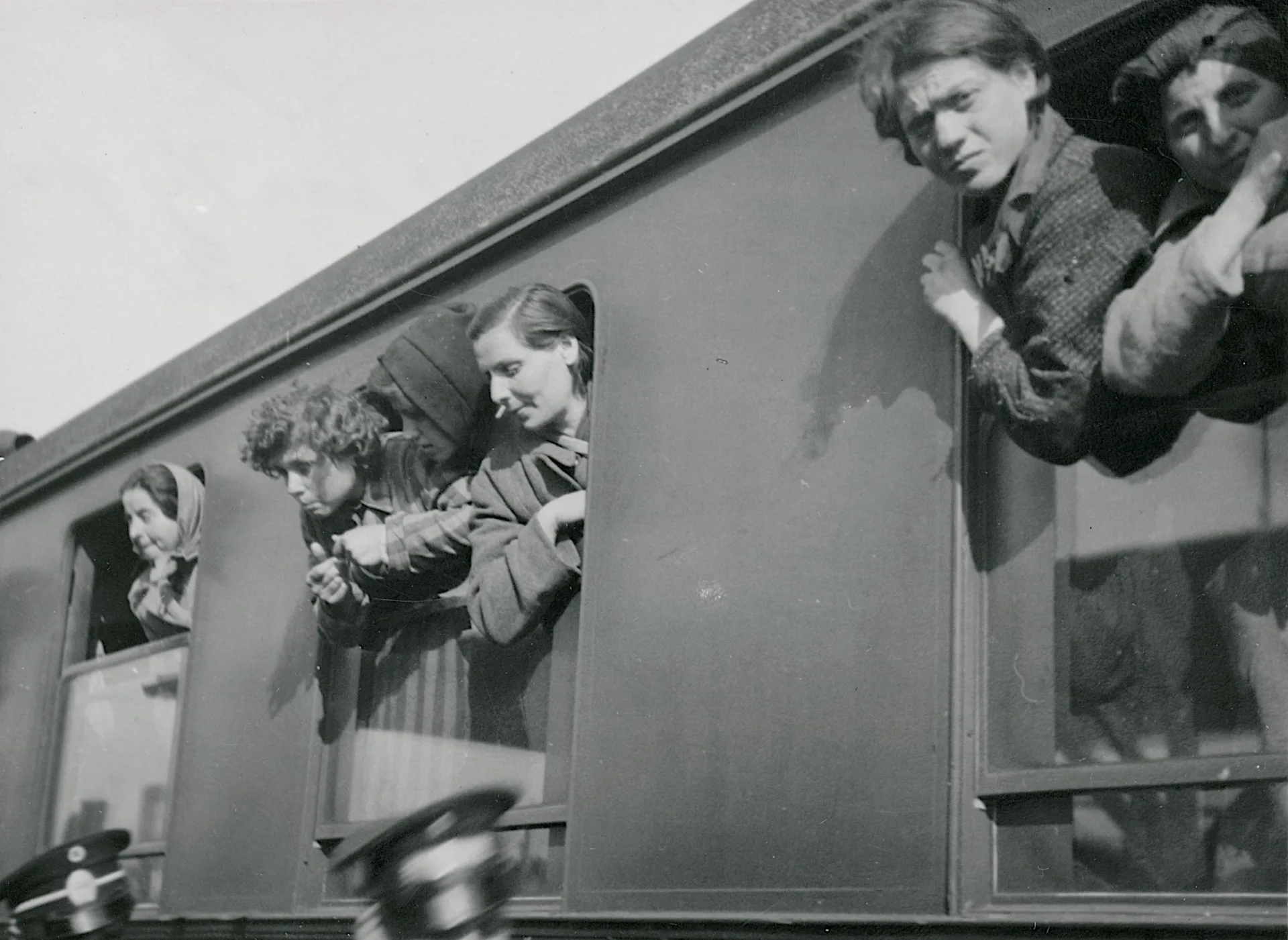 Personer som sticker ut sina huvuden ur fönsterna på en tågvagn.