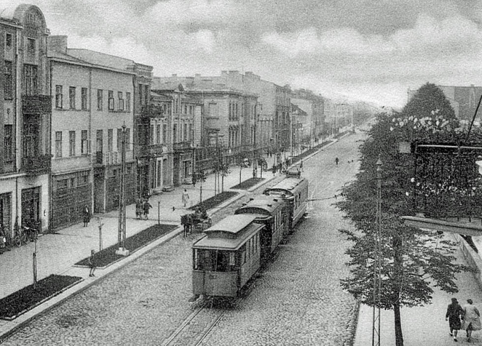 Gatubild Pabianice 1926, till vänster i bild syns höghus, i gatan en spårvagn och en häst och vagn. På trottoarerna promenerar människor.