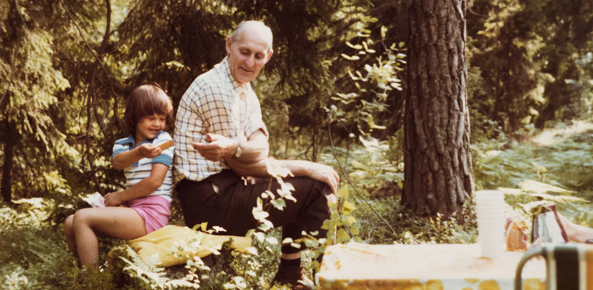 Sommarbild på Czeslaw Aredzki i en skog sittandes intill ett barn.