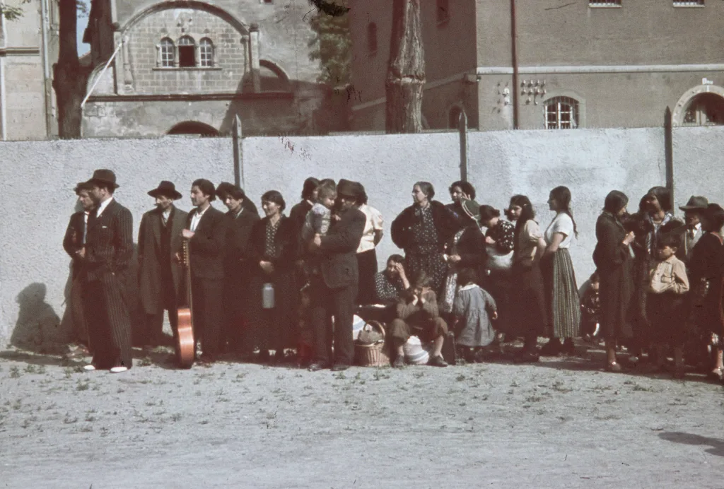 Romska fångar väntar framför en mur.