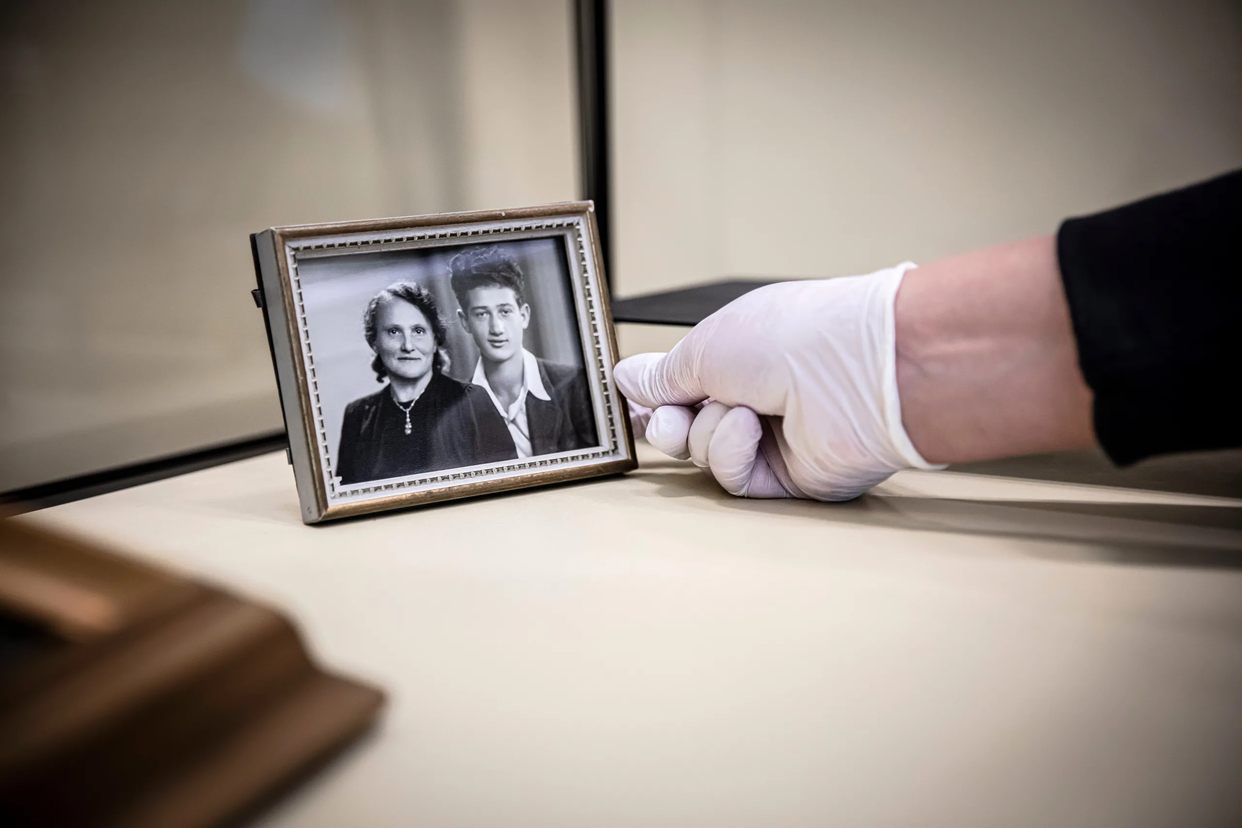 En hand med vit handske placerar en ram med ett svartvitt fotografi i en monter på museet.