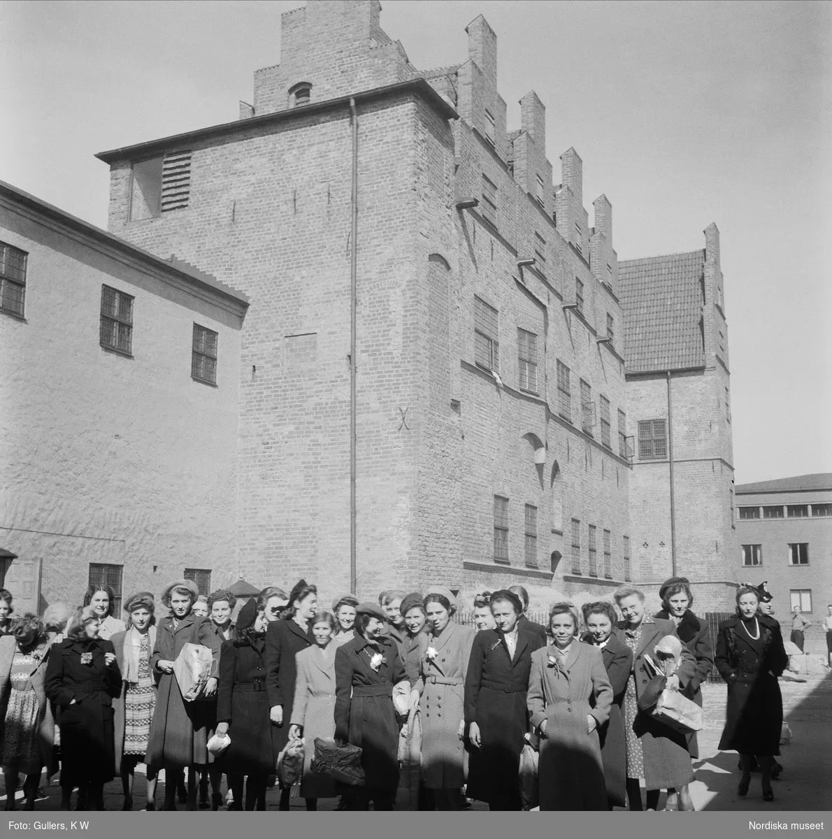Ett stort hus i bakgrunden och flera personer ståendes med ansiktena mot kameran.