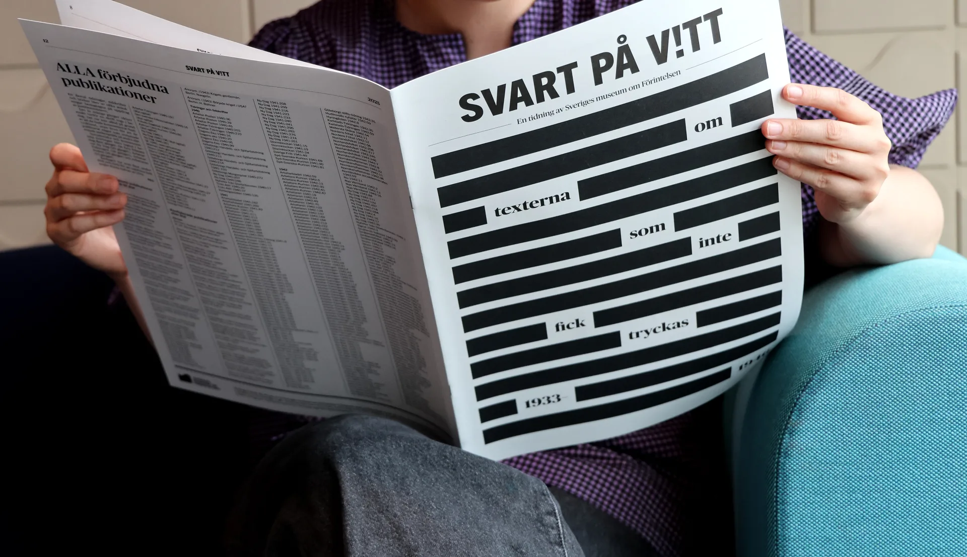 En person sittande i en soffa läsandes en tidning. Huvudet och fötterna syns inte.