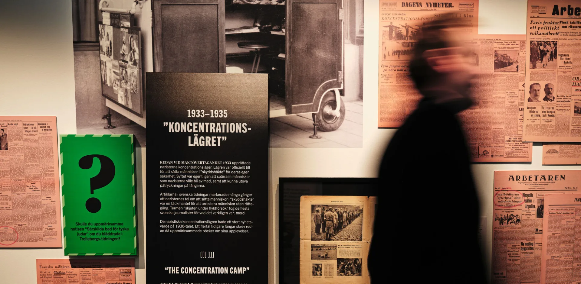 A person in the exhibition In Black and White, newspapers in the background.