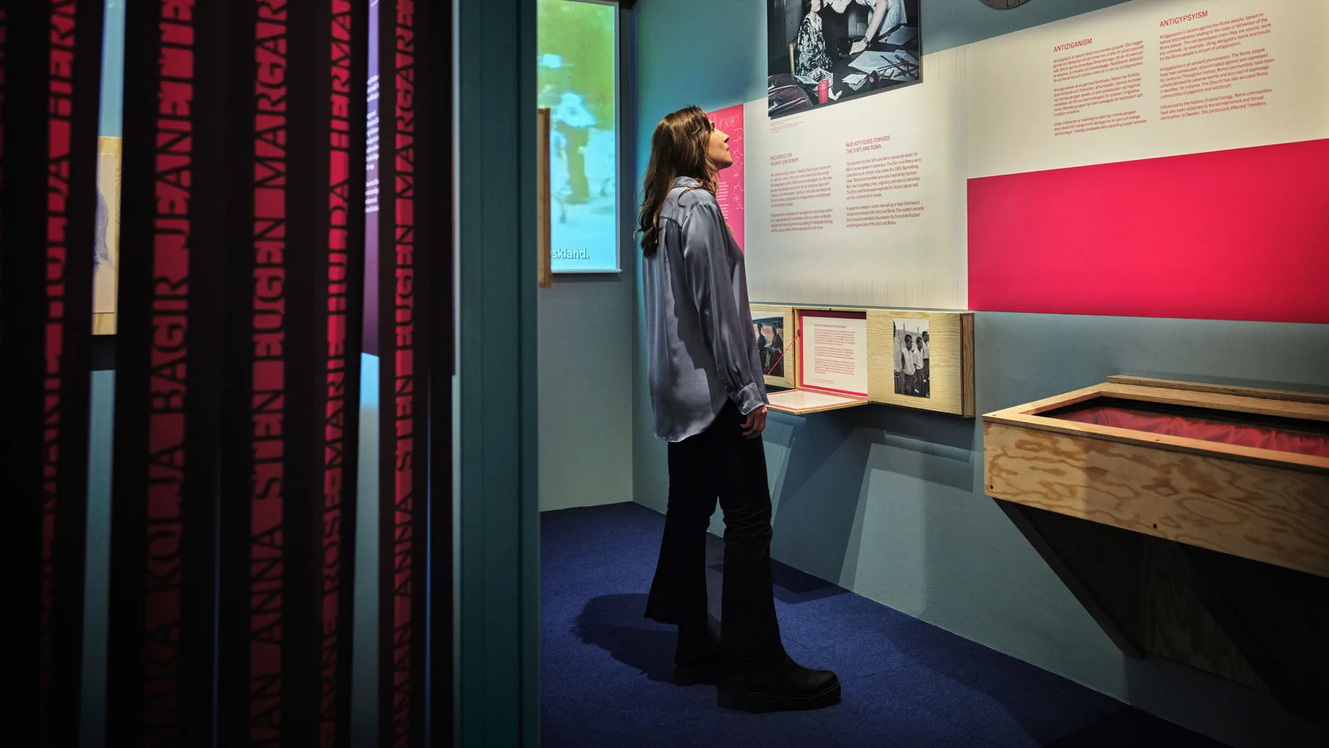 Vy mot utställningen Oberättat där montrar och ett draperi syns, en person läser vid en vägg.