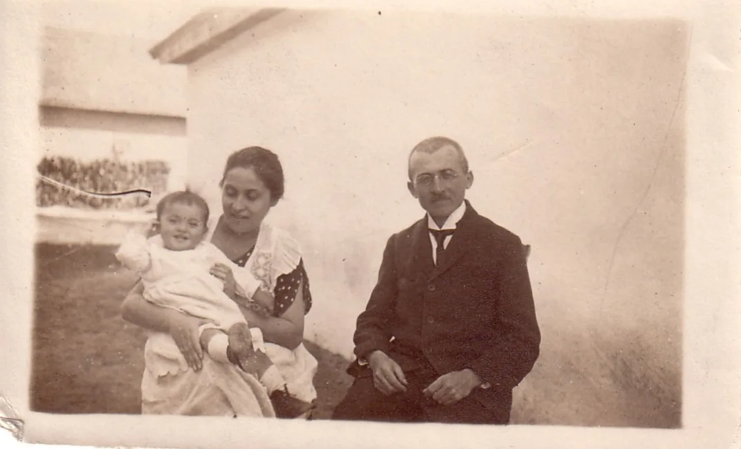 Svartvit bild från 1921 av Vera och hennes föräldrar som sitter utomhus vid en husfasad.