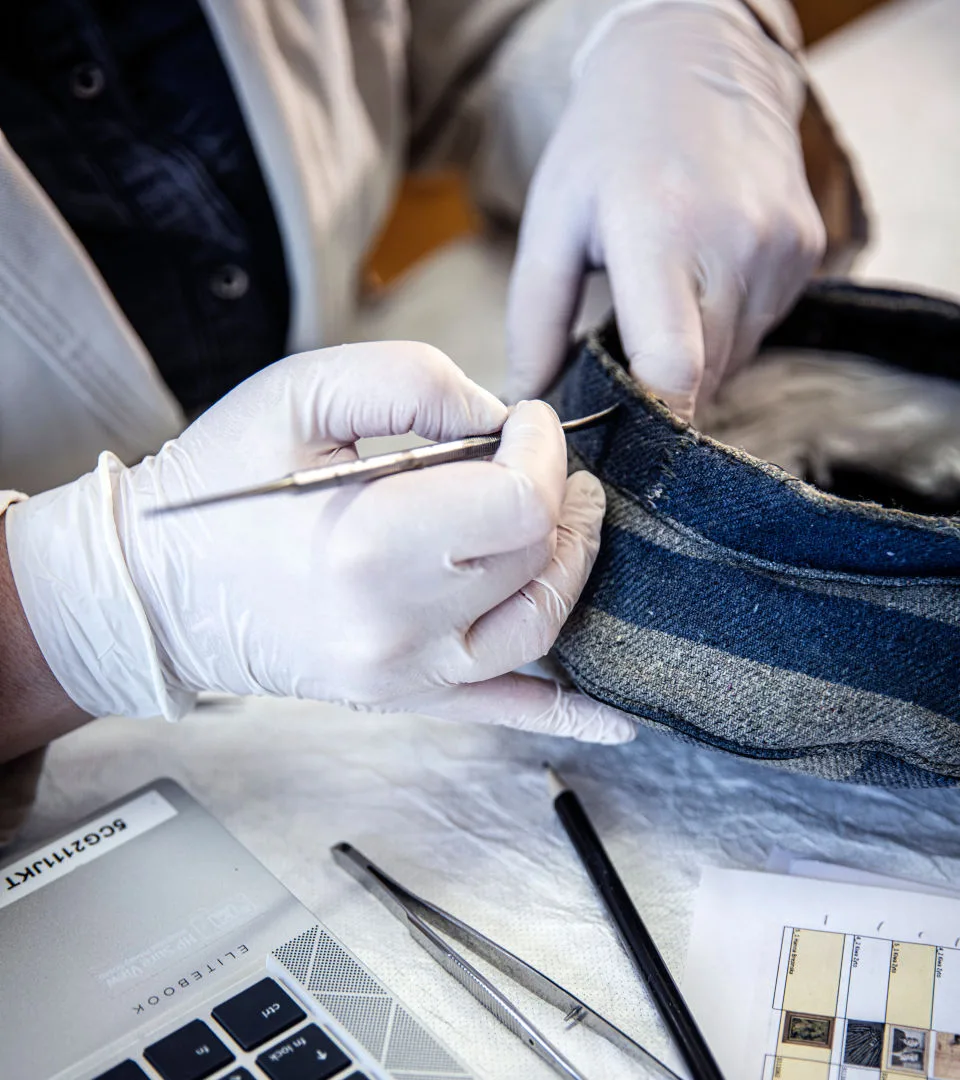 Person med vitklädda handskar hanterar ett föremål i museets samling.