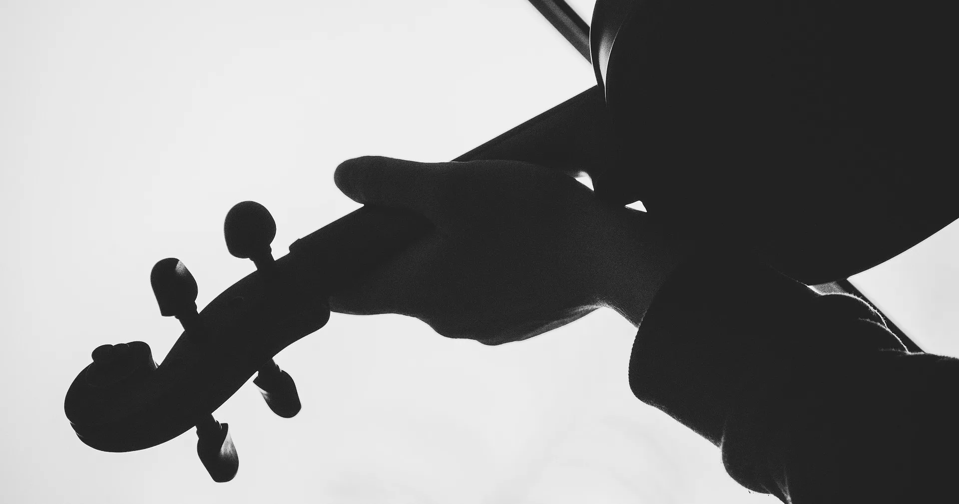 Svart siluett av en hand som håller i ett stråkinstrument.